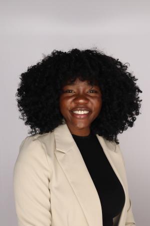 A woman in professional dress in front of a blank wall.